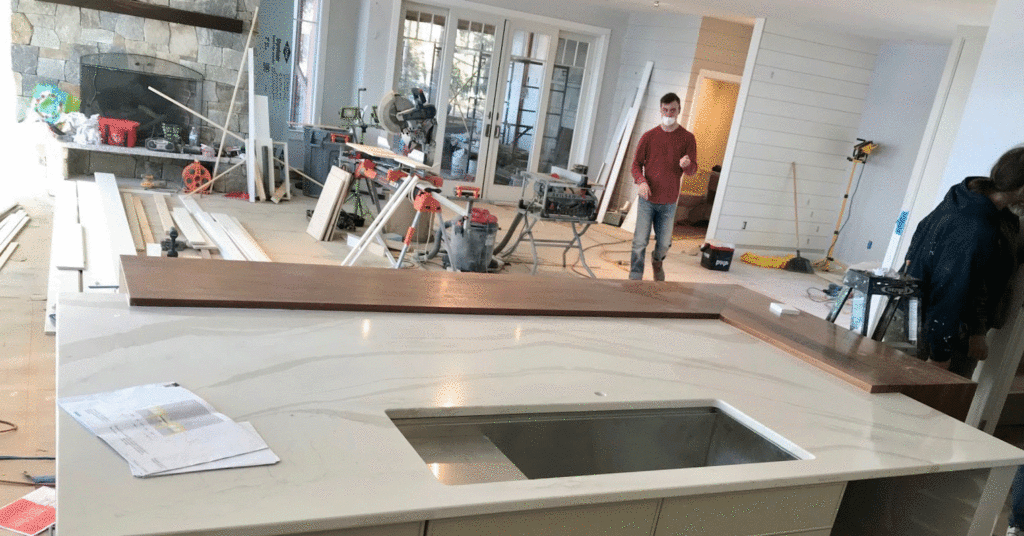 Residential kitchen installation with a large stone island in the foreground and an employee in the background with tools